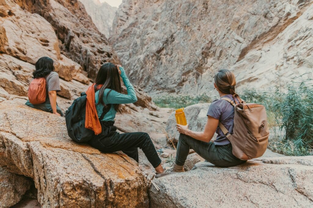 Three women sit on rocks together overcoming impostor syndrome women