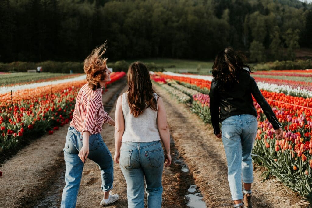 Three women walk together in tulip field laughing and smiling